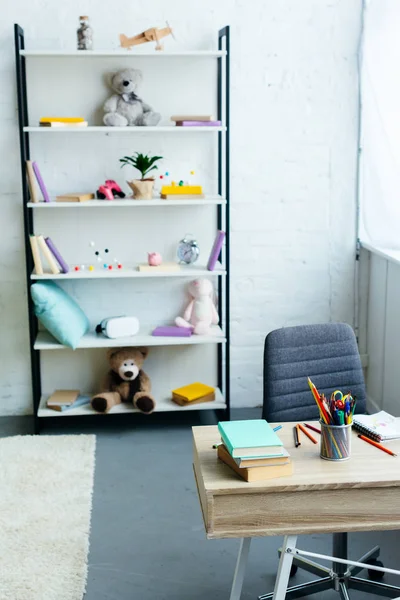 Libri e giocattoli su scaffali e tavolo in legno con materiale scolastico — Foto stock