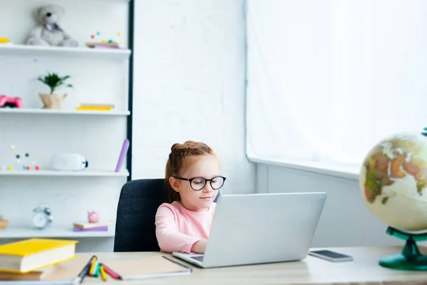 Bella studentessa dai capelli rossi che utilizza il computer portatile mentre studia a casa — Foto stock