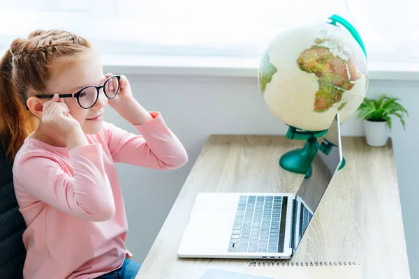 Bonito sorrindo criança usando laptop enquanto sentado na mesa — Fotografia de Stock