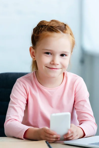 Belle rousse enfant en utilisant smartphone et souriant à la caméra — Photo de stock