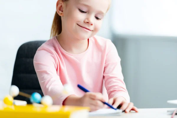 Обрезанный снимок милой улыбающейся школьницы, делающей заметки — стоковое фото
