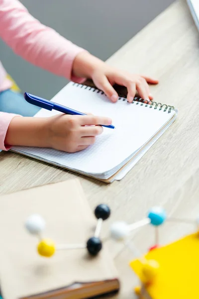 Обрезанный снимок школьника, делающего заметки во время учебы с книгами и молекулярной моделью — стоковое фото