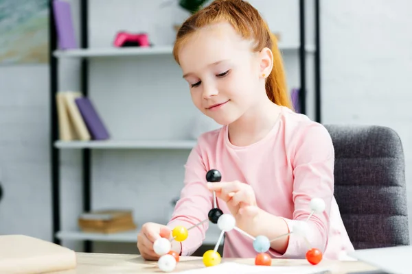 Belle sourire rousse écolière étudiant avec modèle moléculaire à la maison — Photo de stock