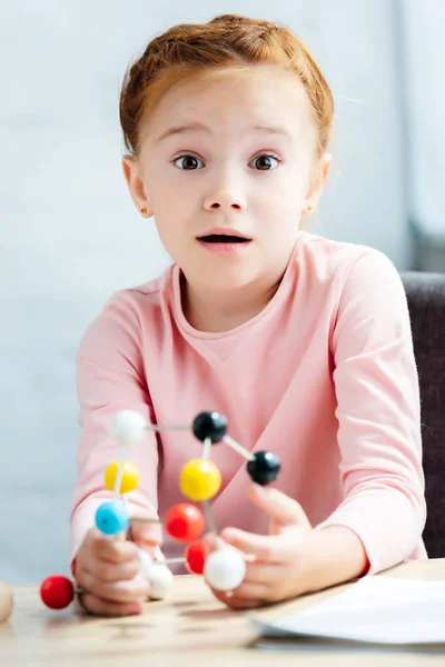 Niño sorprendido sosteniendo el modelo molecular y mirando a la cámara - foto de stock
