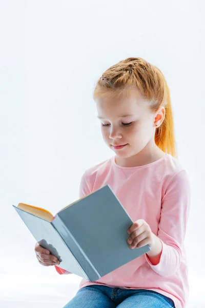 Adorable rojo pelo niño lectura libro mientras sentado en ventana alféizar - foto de stock