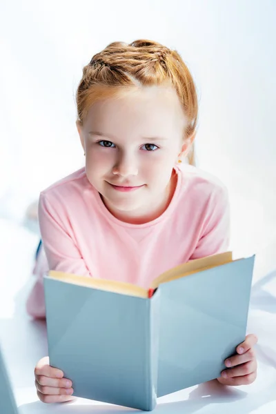 Entzückendes Kind mit Buch in der Hand und lächelnd in die Kamera — Stockfoto