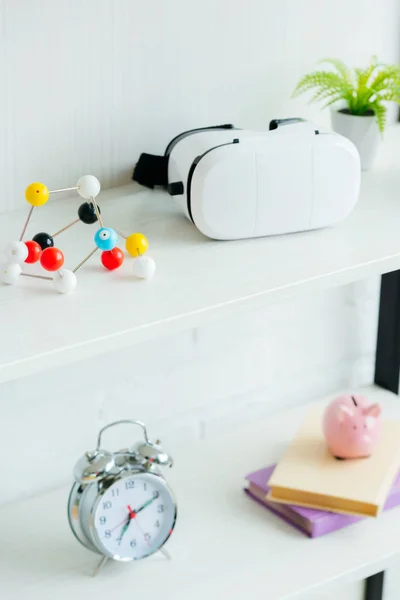 Close-up view of molecular model, virtual reality headset and books on shelves — Stock Photo