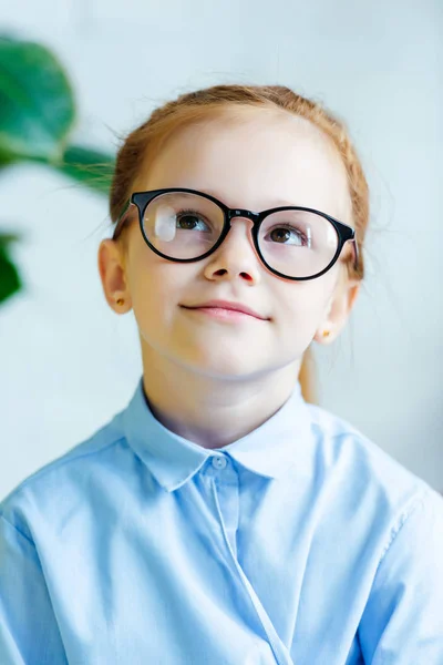 Ritratto di una bella bambina rossa con gli occhiali che sorride e alza lo sguardo — Foto stock