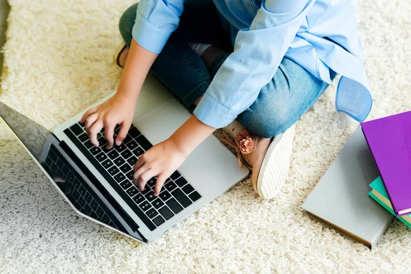 Обрезанный снимок маленького ребенка, сидящего на ковре и использующего ноутбук с чистым экраном дома — стоковое фото