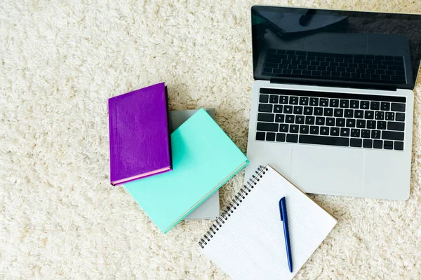 Vista superior de libros, cuaderno con pluma y portátil con pantalla en blanco en la alfombra - foto de stock