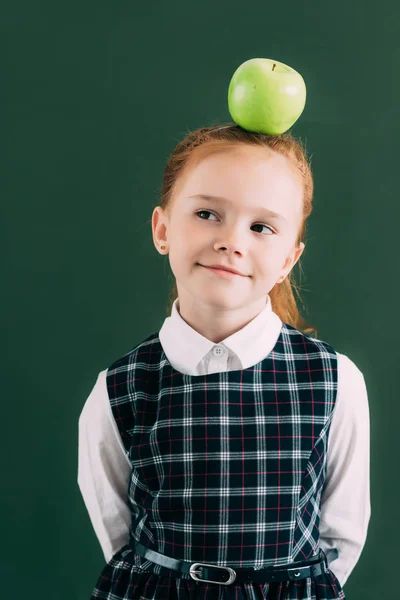 Sorridente piccola studentessa pensierosa con mela in testa guardando altrove — Foto stock