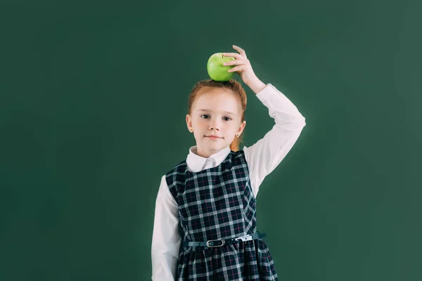 Bella piccola studentessa dai capelli rossi con mela sulla testa guardando la fotocamera — Foto stock