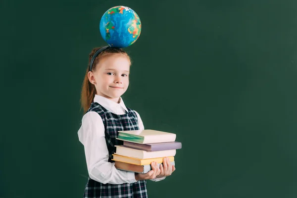 Bella scolaretta con globo sulla testa che tiene mucchio di libri e sorride alla macchina fotografica — Foto stock