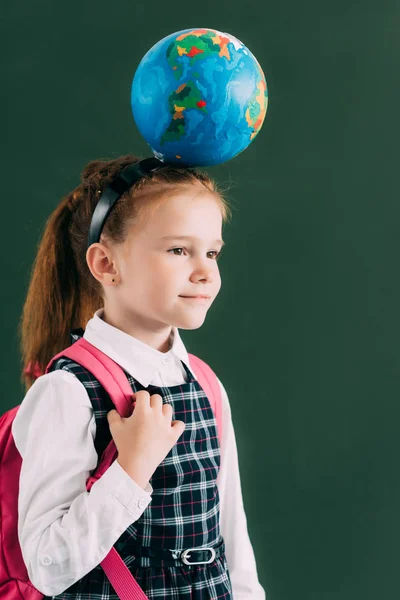 Adorable colegiala con mochila y globo en la cabeza mirando hacia otro lado - foto de stock