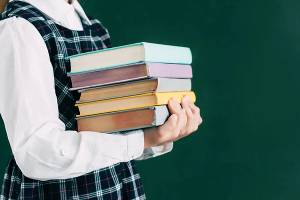 Cropped shot of schoolgirl holding pile of books while standing near blackboard — Stock Photo