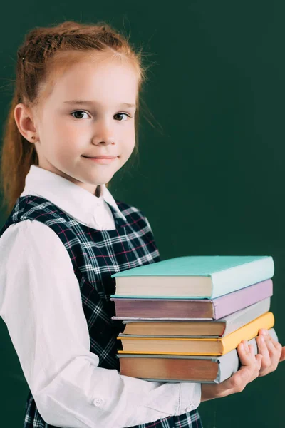 Entzückendes kleines Schulmädchen, das einen Stapel Bücher in die Kamera lächelt — Stockfoto