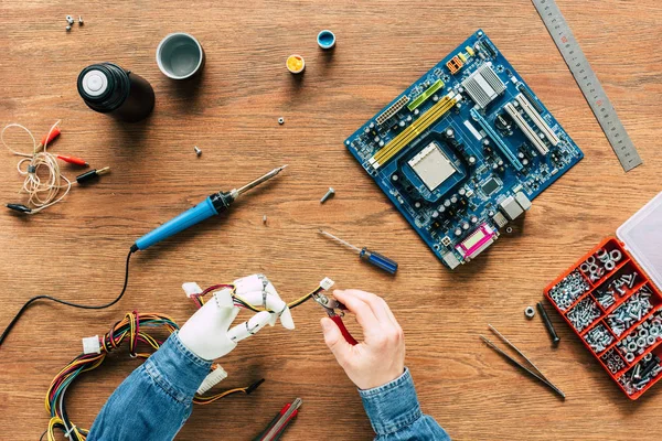 Abgeschnittenes Bild eines Mannes mit Roboterhand, der Drähte mit der Zange über den Tisch schneidet — Stockfoto