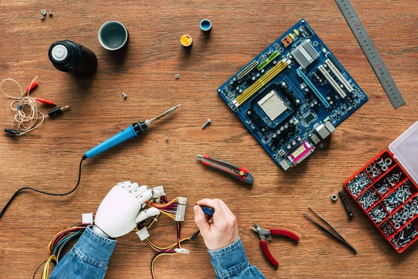 Cropped image of man with prosthetic arm repairing wires by screwdriver at wooden table — Stock Photo