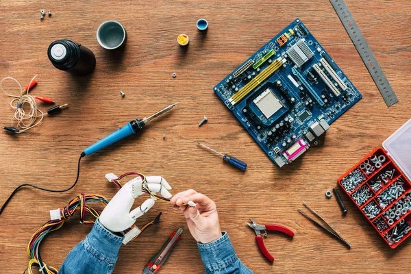 Imagen recortada del hombre con cables robóticos de mano con herramientas en la mesa de madera - foto de stock