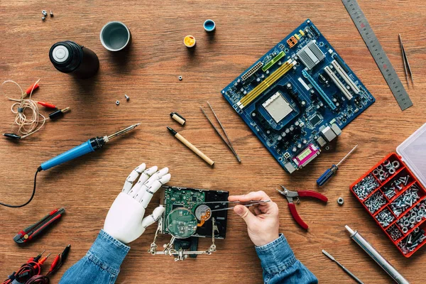 Cropped image of man with robotic hand repairing hard drive by tweezers — Stock Photo