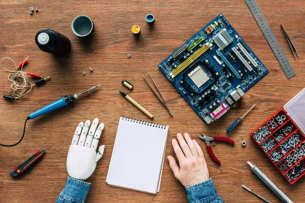 Abgeschnittenes Bild eines Mannes mit prothetischem Arm am Tisch mit Lehrbuch, Instrumenten und Motherboard — Stockfoto