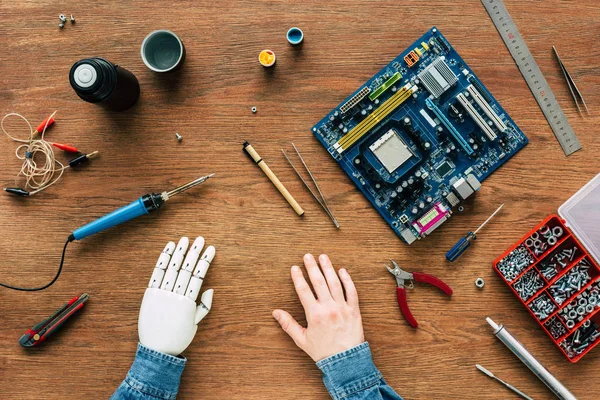 Imagem cortada do homem com o braço protético sentado à mesa com instrumentos — Fotografia de Stock