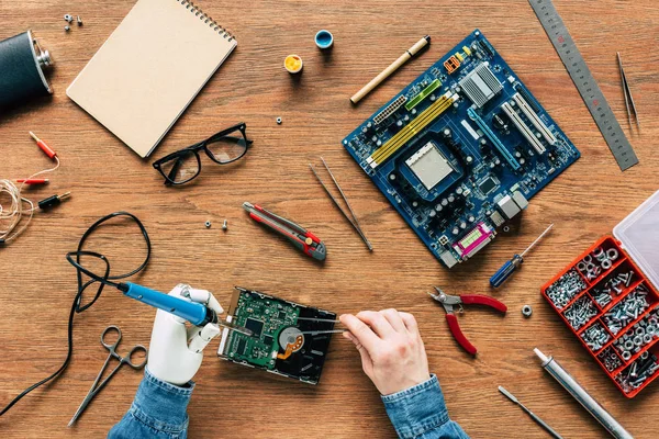 Zugeschnittenes Bild eines Elektronikers mit Roboterhand-Lötwerkzeug am Tisch — Stockfoto