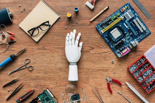 Top view of prosthetic arm on wooden table with tools, spectacles and textbook — Stock Photo