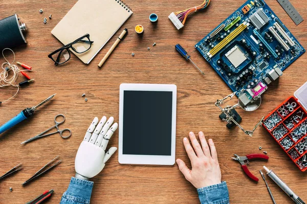 Imagem recortada de engenheiro eletrônico com sittng mão robótica à mesa com tablet digital cercado por ferramentas — Fotografia de Stock