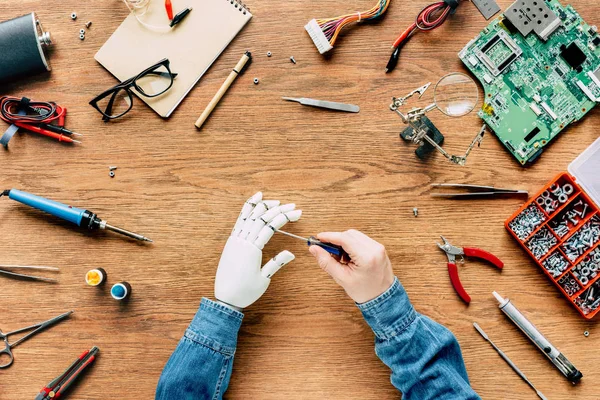 Cropped image of man fixing prosthetic arm by screwdriver at wooden table — Stock Photo