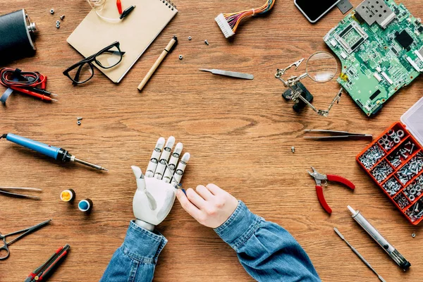 Immagine ritagliata dell'uomo che fissa la mano robotica con un cacciavite al tavolo di legno — Foto stock