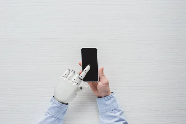 Imagem cortada do homem com mão ciborgue usando smartphone com tela em branco sobre mesa de madeira — Fotografia de Stock