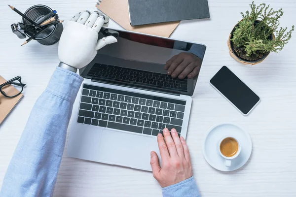 Vista parziale dell'uomo d'affari con computer portatile di apertura del braccio protesico a tavola in ufficio — Foto stock