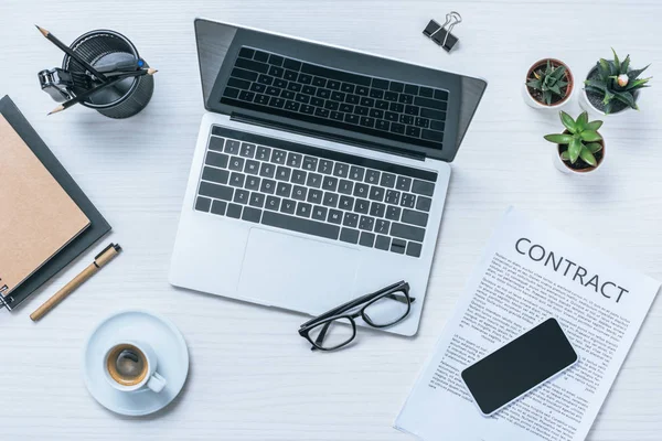 Top view of laptop with blank screen, eyeglasses and smartphone over contract paper at table — Stock Photo