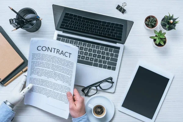 Imagen recortada de hombre de negocios con contrato de lectura de brazo protésico en la mesa en la oficina - foto de stock