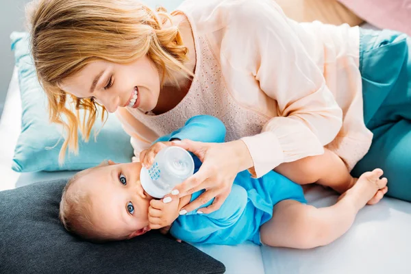 Mother feeding her little child with baby bottle while lying on bed at home — Stock Photo