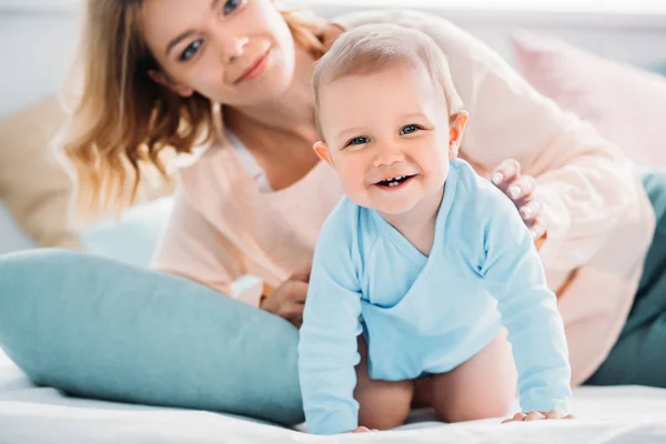 Mutter und glückliches kleines Kind schauen gemeinsam in die Kamera, während sie es sich im Bett gemütlich machen — Stockfoto