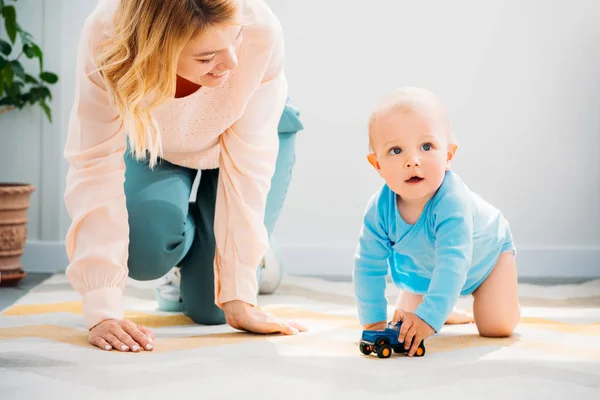 Madre e hijo arrastrándose juntos en la alfombra en casa - foto de stock