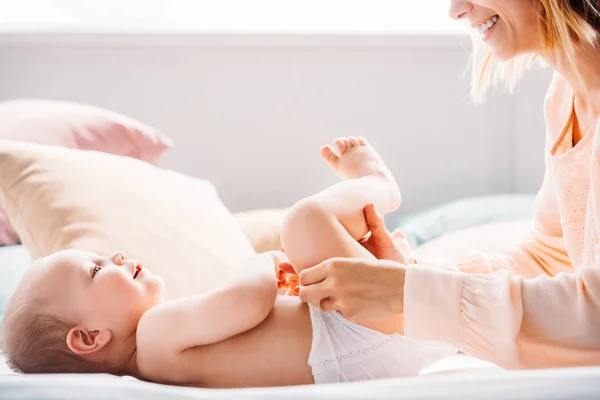 Tiro cortado de mãe feliz colocando fralda em criança enquanto ele brincava com brinquedo — Fotografia de Stock