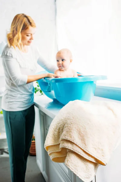 Madre joven bañando al niño en la bañera de plástico en casa - foto de stock