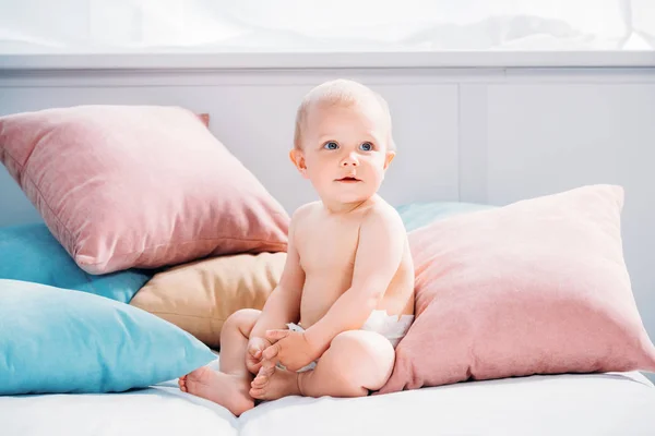 Bebê pequeno feliz sentado na cama com muitos travesseiros e olhando para cima — Fotografia de Stock