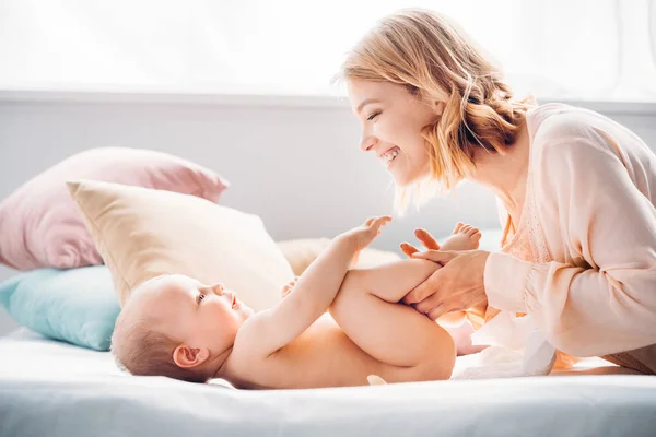 Feliz madre poniendo pañal en el niño pequeño en la cama - foto de stock