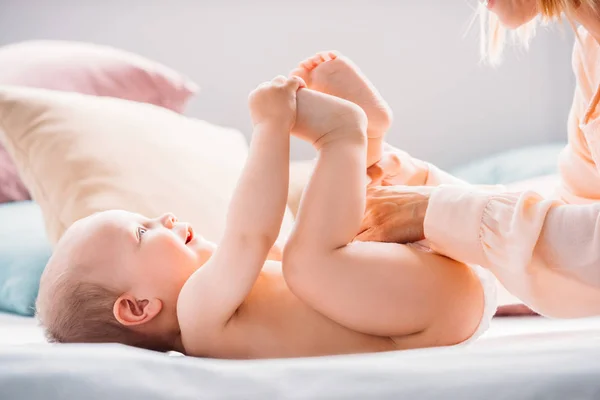 Colpo ritagliato di madre che mette il pannolino sul bambino piccolo mentre ride — Foto stock