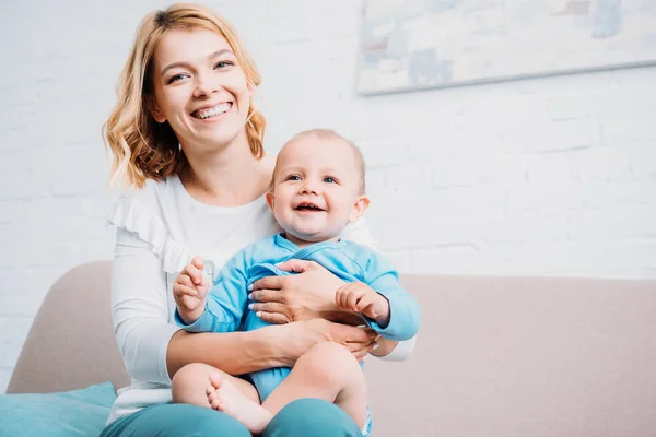 Happy mother embracing little child while sitting on couch at home — Stock Photo