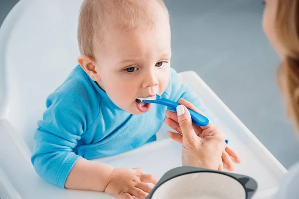 Schnappschuss von Mutter, die entzückendes Kind mit Haferbrei füttert — Stockfoto