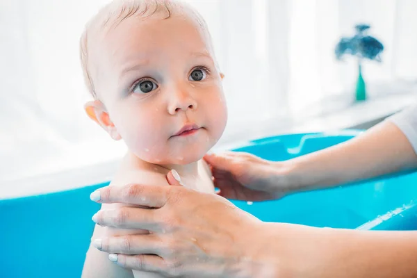 Recortado tiro de madre lavando su hermoso niño en plástico bañera de bebé en casa - foto de stock