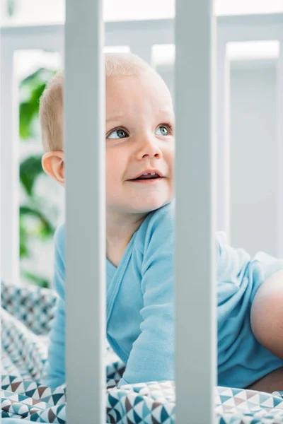 Adorable little baby lying in crib and looking away — Stock Photo