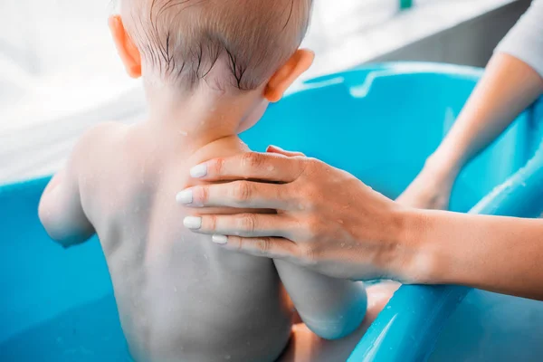 Recortado tiro de la madre lavando a su hijo en plástico bañera de bebé en casa - foto de stock