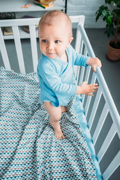 High angle view of cute little baby standing in crib — Stock Photo