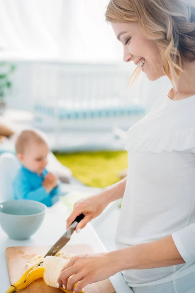 Mother cutting banana to make porridge for her child sitting blurred on background — Stock Photo